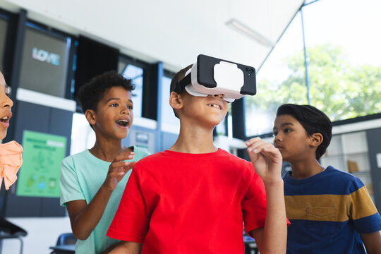 Three biracial boys are exploring virtual reality in the classroom at school, one wearing a VR heads