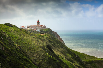 Fototapeta na wymiar Cabo da Roca western point of Europe in Portugal at Atlantic Ocean photo during a beautiful sunny day. Amazing color of ocean water, view to lighthouse. Travel to Portugal.