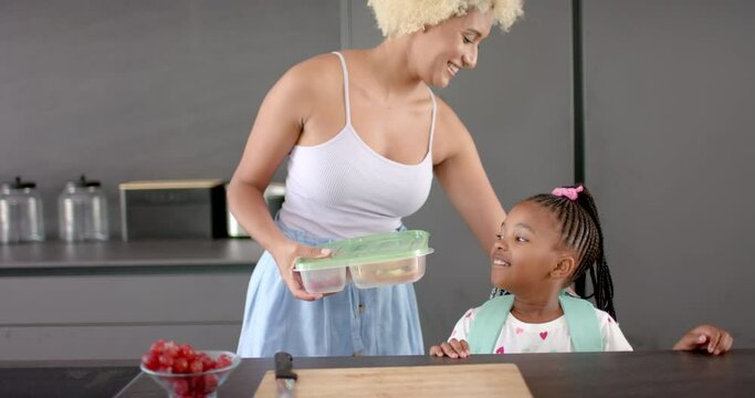 Biracial mom and daughter share a moment in kitchen with fruit.