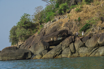 Two adults doing photography at a hill near butterfly beach in Goa, India. Huge rocks and green...