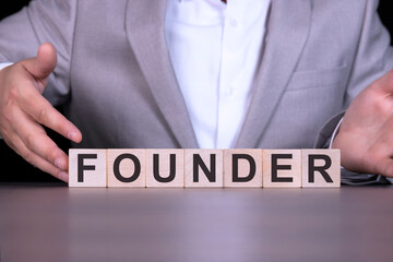 FOUNDER, the word is written on wooden cubes, blocks on the background of a man, a businessman in a gray suit.