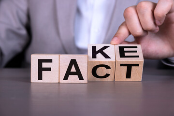 Naklejka premium A businessman's hand turns over wooden cubes to change the wording from fake to fact.