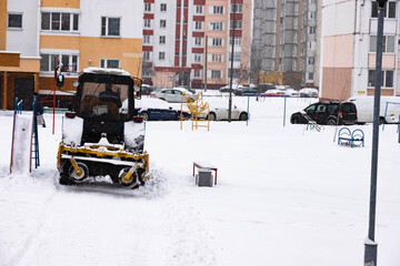 The tractor clears the road from snow in winter during a snowfall.
