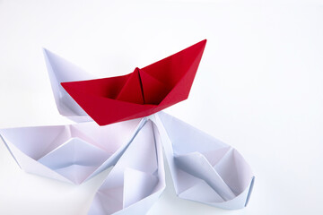 one red paper boat between many white paper boats. Copy space.