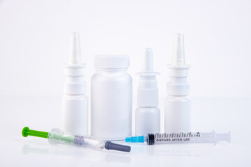 Nasal sprays, syringes, white medical jar for pills on a white background Concept of treatment of flu, virus, cold. Copy space.