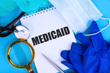 MEDICAID, text written in a notebook lying on a blue background, with a stethoscope and a medical...