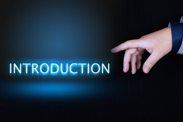 INTRODUCTION text, word written in neon letters on a black background pointed to by a hand with a person's index finger.