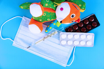 Protective medical mask with toy fox, thermometer and pills on a blue background. School quarantine concept, home schooling