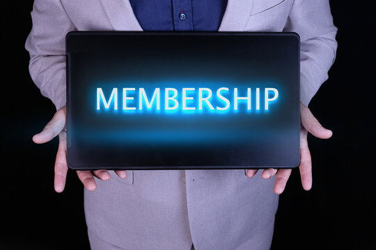 MEMBERSHIP word, text written in neon letters on a laptop which is being held by a businessman in a gray suit.