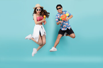 Happy Asian couple jumping and using water guns on blue background. Songkran Festival in Thailand