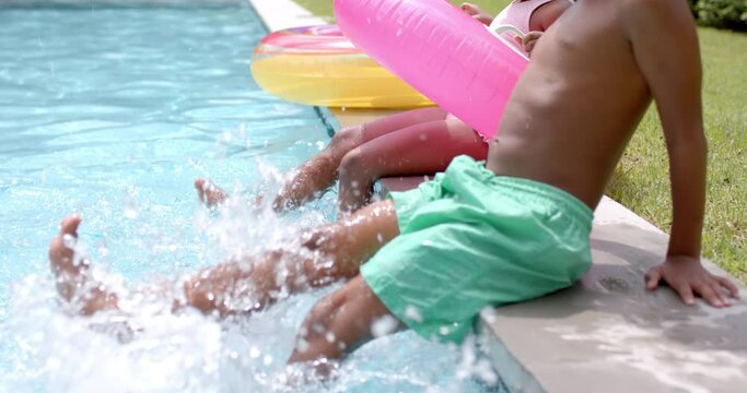 African American siblings splash water by a poolside at home, with a pink float nearby