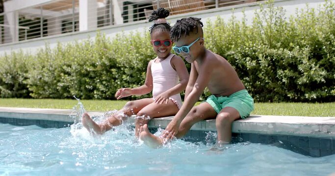 African American sister and brother enjoy poolside fun at home, splashing water with their feet