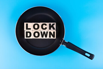 LOCKDOWN word, text written on wooden cubes, building blocks lying in a frying pan, and blue...