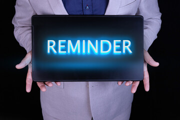 REMINDER text, word written in neon letters on a black laptop, in front of a businessman in a gray suit.