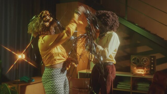 Happy African-American couple in fashionable outfits dancing with silver tinsel on retro party in studio with vintage interior. Zoom shot, retro glow effect