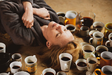 Woman surrounded by many cups of coffee, deadline concept. Workaholism, overtime, the need to be...