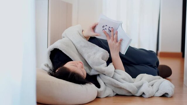 wellness and wellbeing concept with asian woman lie down and read book in livingroom