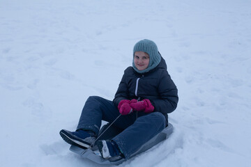 Fototapeta na wymiar A satisfied modern child in a plastic sled rides down the mountain