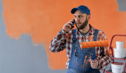 house painter man calling on mobile phone, holding paint roller, making home renovation