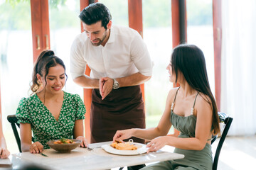 Waitress man serving food to group of diverse customer in restaurant, eatery client woman and man having smile and happy with service mind from cafes staff, lunch or dinner time lifestyle with family