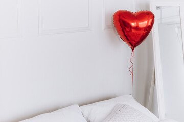 Inflatable foil red heart shaped air balloon on white background tied to a bed. Valentine`s day concept celebration decoration in photo studio. Love, holiday, party
