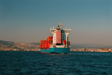 Cargo ship loaded with containers, leaving the port towards the city on the opposite shore