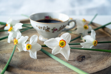 Still life with a delicate decoration of white daffodil flowers around a baroque fine porcelain coffee cup on a wooden tray - 756269026