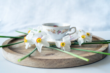 Still life with a delicate decoration of white daffodil flowers around a baroque fine porcelain coffee cup on a wooden tray - 756269091