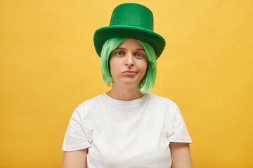 Boring St. Patrick's Day celebration. Sad unhappy upset woman wearing festive green hat standing isolated over yellow background looking at camera with displeased expression