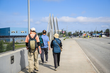 Three people walking on a pedestrian footpath along the highway. Anchorage. Alaska. USA.