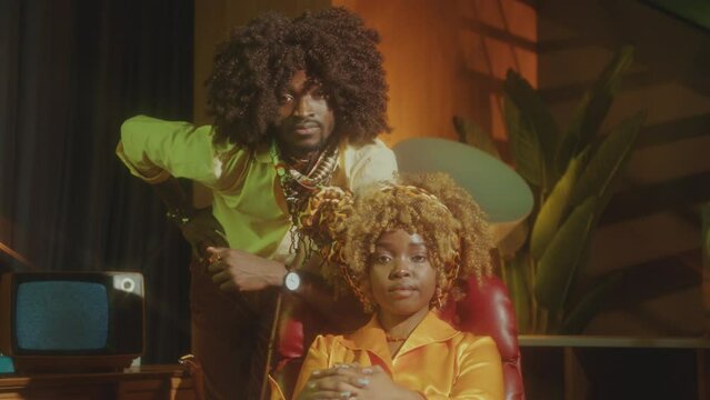Young African American couple in retro glam outfits posing together at camera in vintage studio. Video portrait, zoom shot