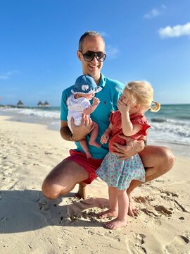 Papa et ses 2 enfants de 2 mois et demi et 4 mois sur la plage devant la mer des caraïbes