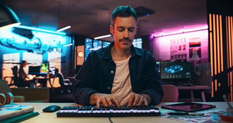 Portrait of a Young Man Typing on Keyboard and Working on Desktop Computer in a Creative Office...