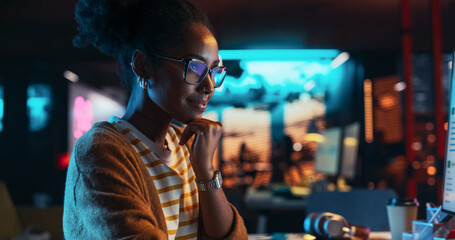 Female Talented Digital Marketing Specialist Working on Computer at Office in the Evening. Young Black Businesswoman in Creative Agency, Smiling and Researching Business Analytical Data