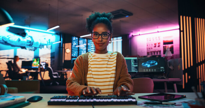 Portrait of a Black Female Developer Writing Code in a Creative Office with Neon Lights. Young Woman Focused on Typing on Keyboard and Working on Desktop Computer. Point of View of Screen Monitor 