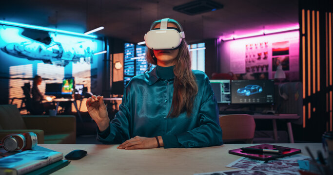 Portrait of Young Adult Female Using Virtual Reality Goggles in Creative Office. Woman Using Futuristic Augmented Reality Software for Managing Business and Marketing Projects