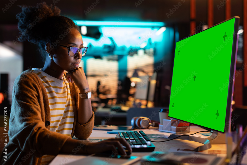 Poster portrait of creative black woman sitting at her desk using desktop computer with mock-up green scree