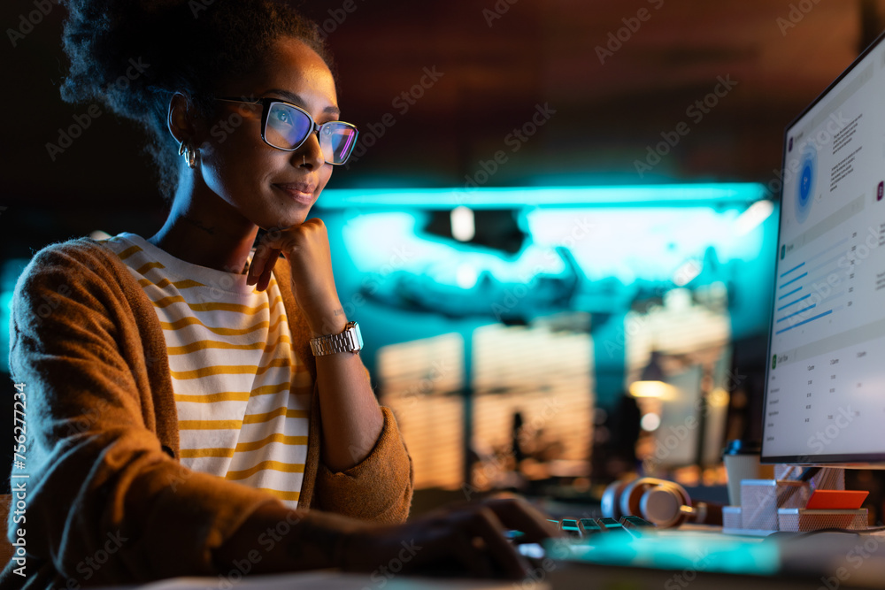 Poster african american female smiling while checking data and statistic charts using desktop computer. por