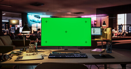 Desktop Computer with Mock Up Green Screen Chroma Key Display Standing on the Desk in the Empty Creative Office Lit by Neon Lights. Monitor in Game Development or Animation Company