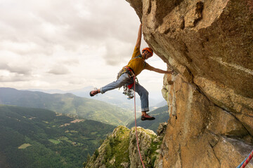 A man is climbing a rock wall with a yellow shirt and orange helmet. Concept of adventure and...