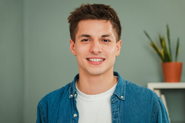 Close up individual portrait of one young adult caucasian guy smiling and looking at camera with friendly expression. Headshot of a real teenage man student with white teeth staring front at home