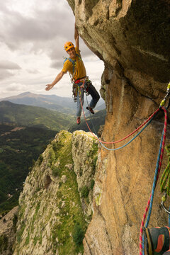A man is climbing a rock wall with a rope attached to him. He is wearing a yellow shirt and a yellow helmet. Concept of adventure and excitement, as the man is taking on a challenging