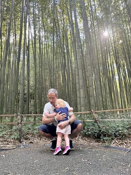 Enfant fille de 1 an et demi dans les bras de son papa devant une forêt de bambous au Japon