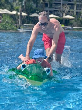 Enfant fille de 1 an et demi jouant sur un crocodile gonflable dans une piscine avec son papa