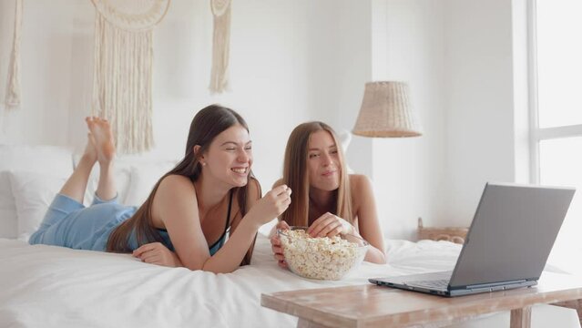 Excited young girls friends watching funny movie on laptop in bedroom