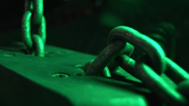 Pulling chain through metal bar detail in green light closeup. Working mechanism of winch hoist in workshop. Industrial equipment scene