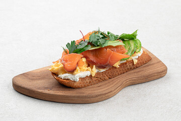 Breakfast toast with salmon and avocado on wooden board