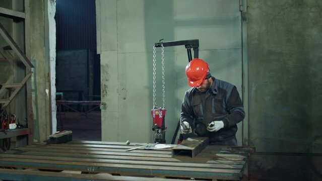 In front of the camera working factory man at the industrial factory he wearing safety equipment using the hammer for work with the metal