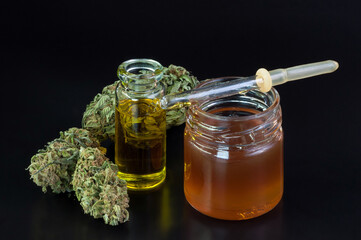 small transparent glass bottle and pipette filled with cannabis oil and dry marijuana flowers around on black background