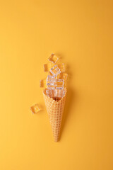 Ice cream cone with ice cubes on yellow background, top view. Creative summer concept. © SOLDATOOFF